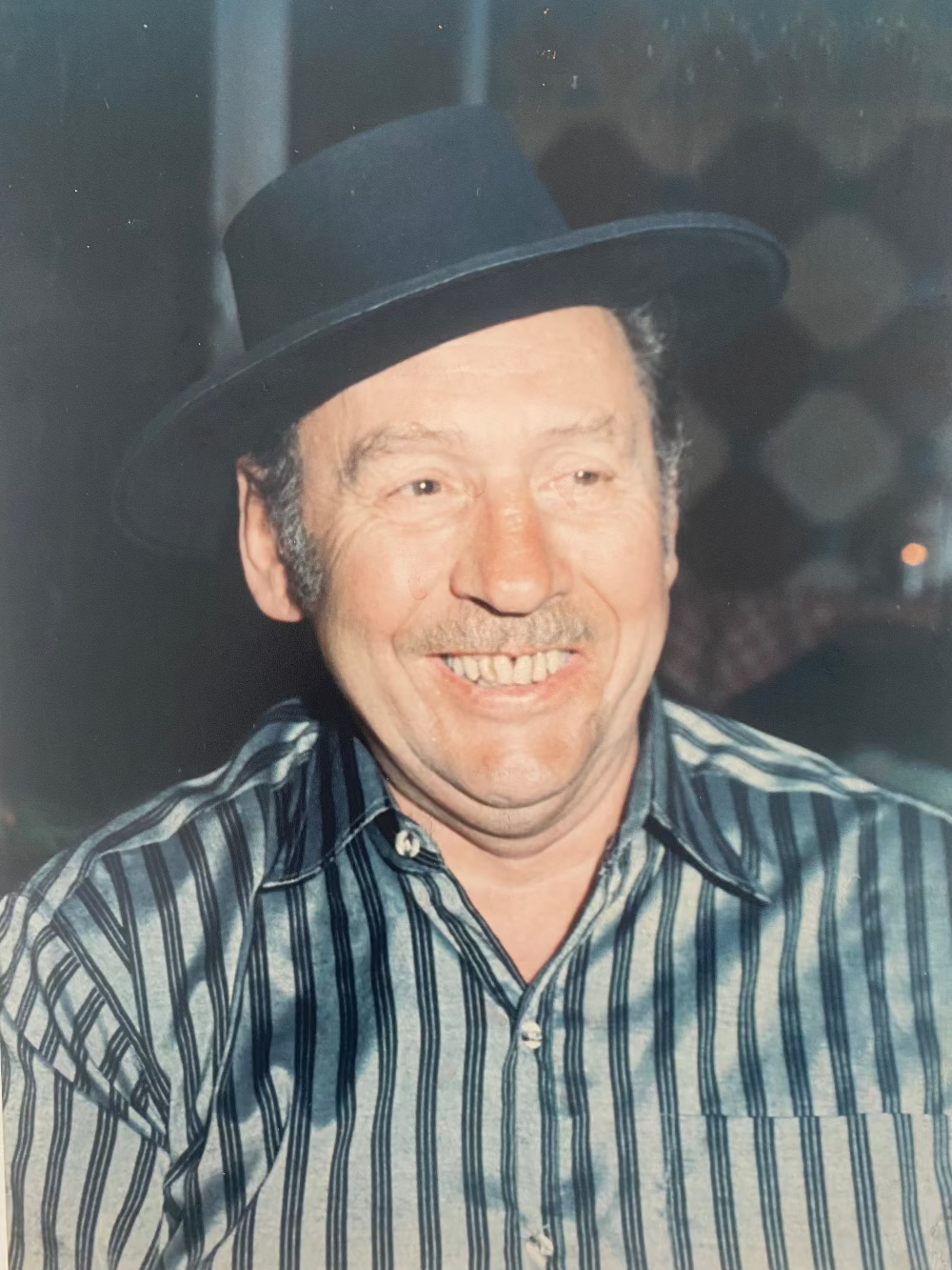 Risto Koch wearing a black hat and striped shirt with a blurred background