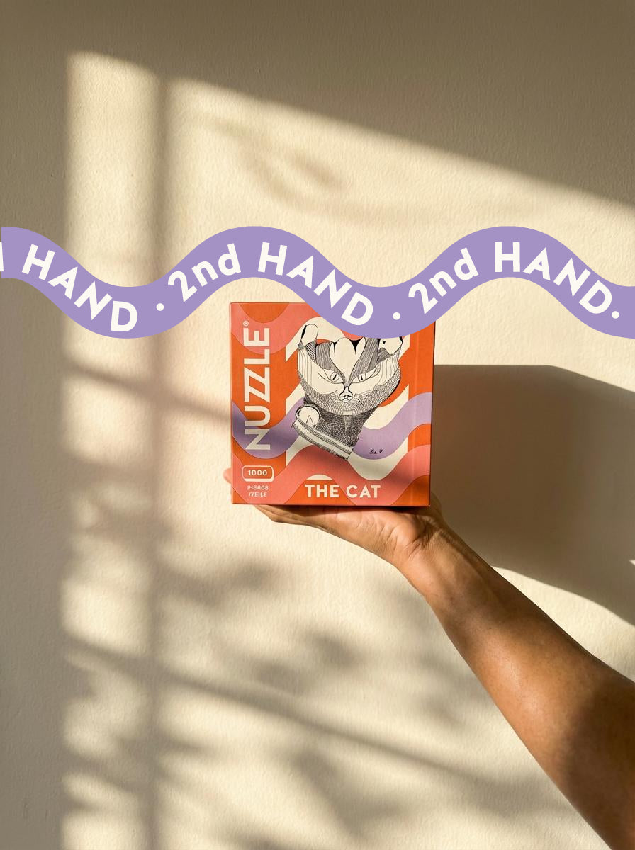 Hand holding a NUZZLE  'The Cat' puzzle against a neutral background with a 2nd hand ribbon